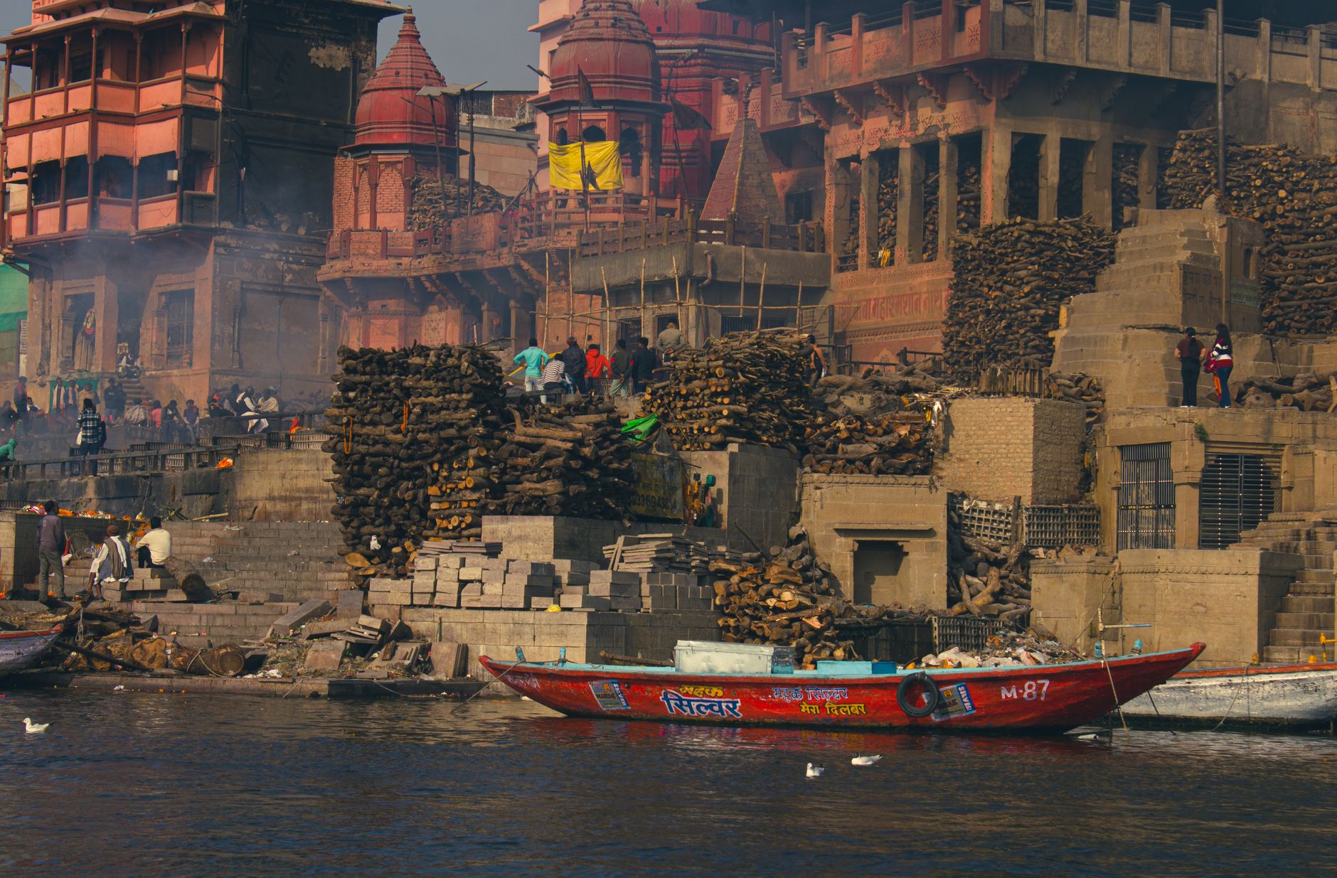 Colorful boats docked by the ancient ghats of Varanasi, with the old city rising behind them.