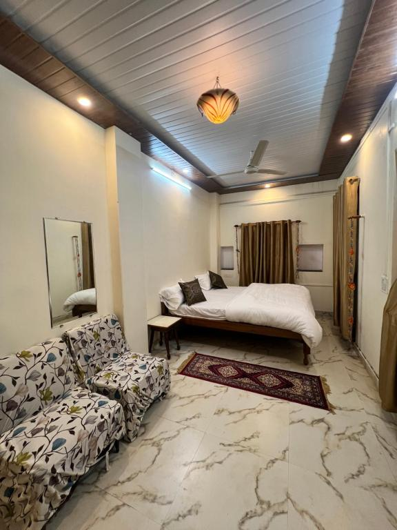 The Premium Room at Krishna Palace, a dressed bed, marble floor and a floral armchair beside a wooden ceiling.